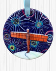 Circular ceramic decoration against a white textured background. It features the Angel of the North on a snowy hill, under a dark sky of colourful fireworks.