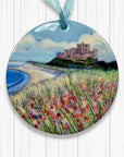 Round ceramic ornament with a Bamburgh castle and floral field and beach design on a white background