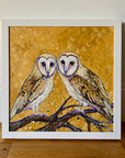 A painting of two barn owls perched on a branch with a leafy ochre beackground.
