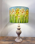 Lamp with floral daffodil design shade on a wooden table against a white wall.