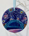 A circular ceramic decoration hung on a white branch. It features the Tyne Bridge under a dark blue sky of colourful fireworks.