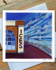 A greetings card featuring the Rendezvous Cafe with the ices signage showing on the building.There is a white lighthouse in the distance. The sky is a cloudy blue with an icy sea.