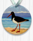 Decorative ornament with a Oyster catcher on a beach design, hanging on a white wooden surface.