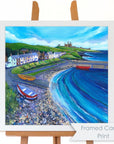 A bright colourful painting of a harbour village in a white frame.