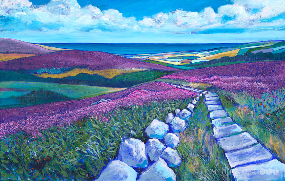Blanketed hills of purple heather aredived by a stone path which lead down to the valley below. in the distance you can see a colourful patchwork of fields with the bright blue sea beyond. f 