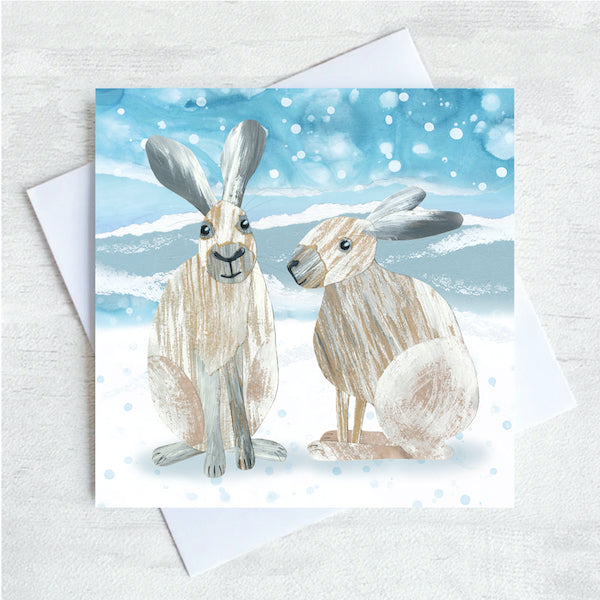 A winter themed greetings card featuring a collage illustration of two winter snow hares in a snow scene.