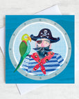 A greetings card featuring a Pirate with a green parrot on his shoulder looking through at the porthole of a ship.