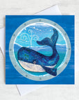 A nautical greetings card featuring a big blue whale as seen through a ships porthole.