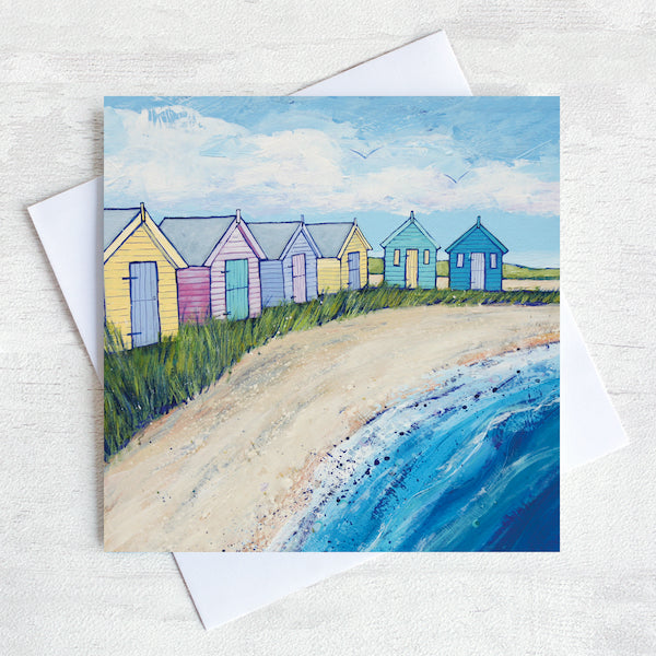 A greetings card featuring a painting of colourful beach huts on a sandy shore.