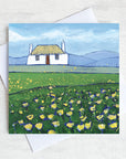 A greetings card featuring a scottish thatched cottage with a field of buttercups in the foreground.