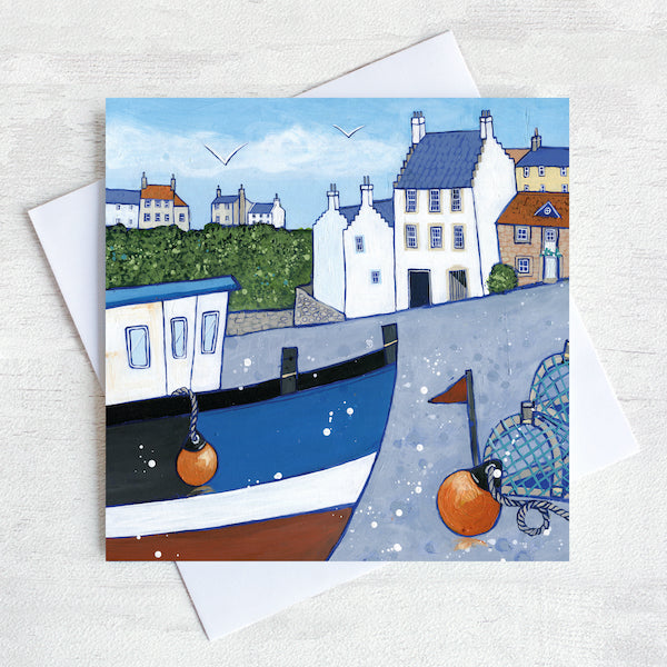 A greetings card featuring a painting of Crail on the Fife coastline. There is a fishing boat in the foreground that is surrounded by creels and lobster pots.
