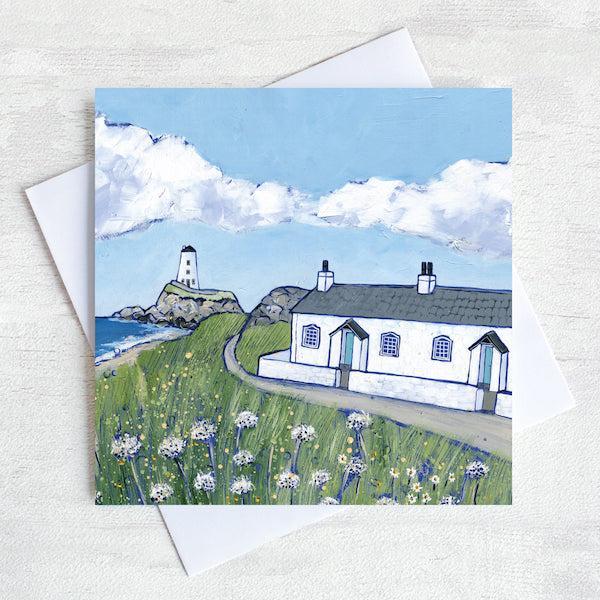 A greetings card featuring the white cottages and lighthouse on llanddwyn island on Anglesey with clover  flowers peppered in the foreground.
