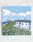 A greetings card featuring the white cottages and lighthouse on llanddwyn island on Anglesey with clover flowers peppered in the foreground.
