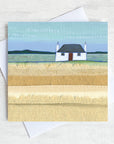 A greetings card featuring a traditional scottish blockhouse with a black roof and a red door. In front is a field of grass.