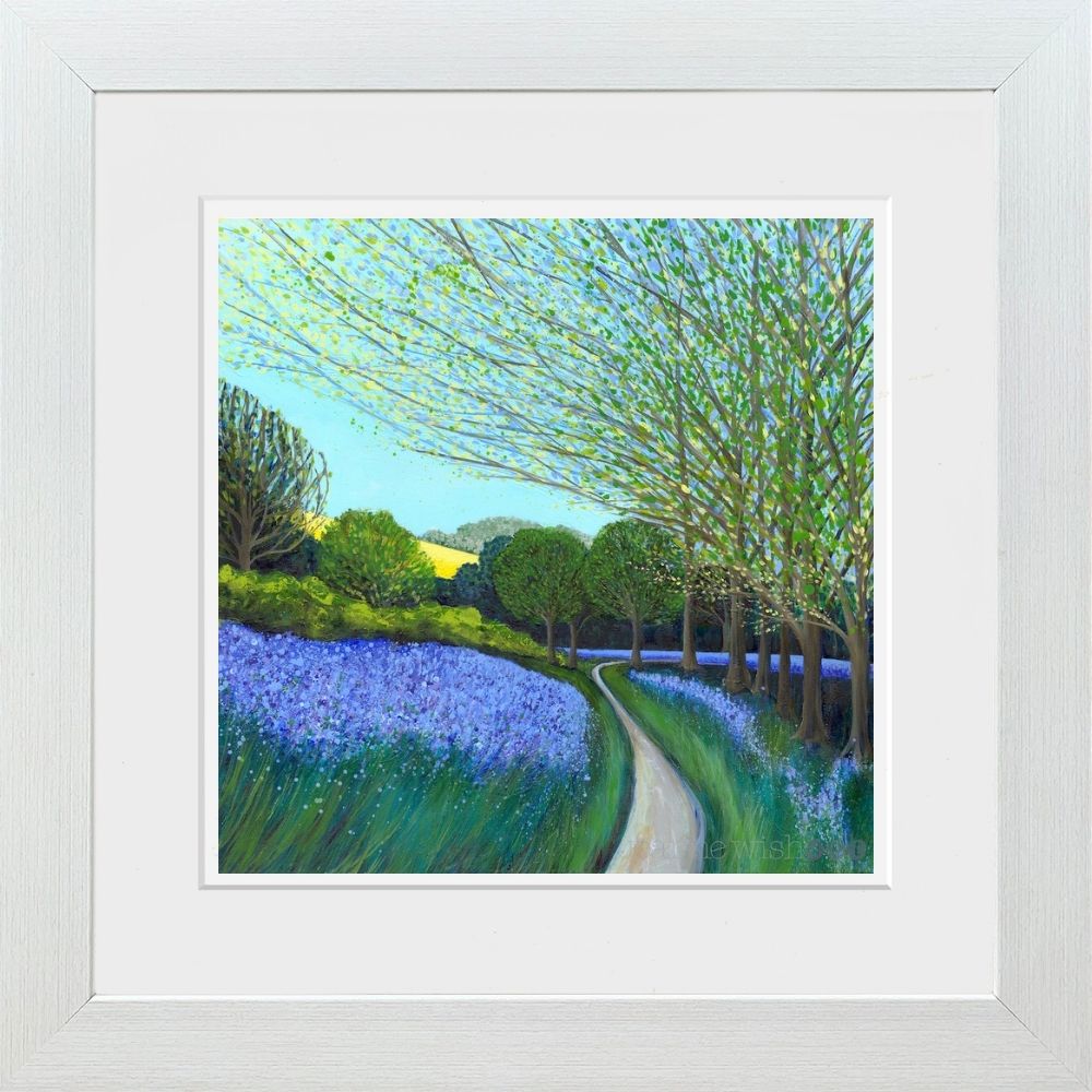 A framed landscape painting featuring a winding path through a field of purple flowers and green trees under a light blue sky, presented in a white frame with a white mat.
