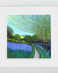A framed landscape painting featuring a winding path through a field of purple flowers and green trees under a light blue sky, presented in a white frame with a white mat.
