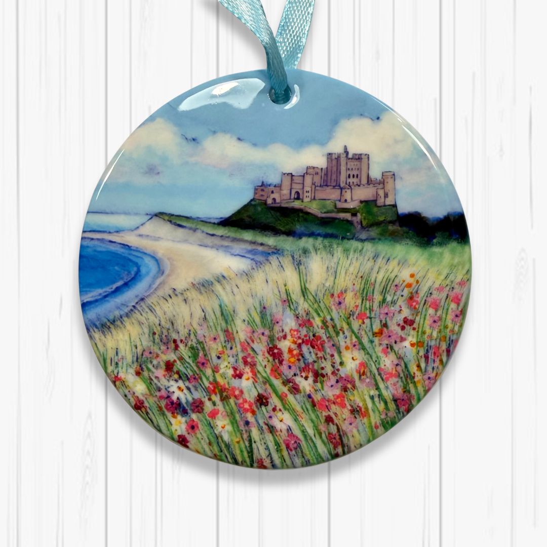 Round ceramic ornament with a Bamburgh castle and floral field and beach design on a white background