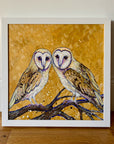 A painting of two barn owls perched on a branch with a leafy ochre beackground. 