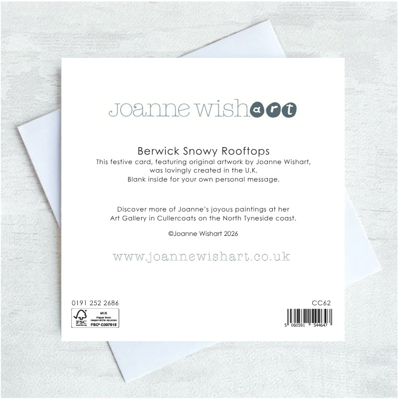 The back of a Joanne Wishart 'Berwick Snowy Rooftops' greeting card, showing printed text and barcode details, displayed on top of white envelopes on a light gray textured background.