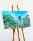 Painting of a landscape with a tree on an easel against a white background