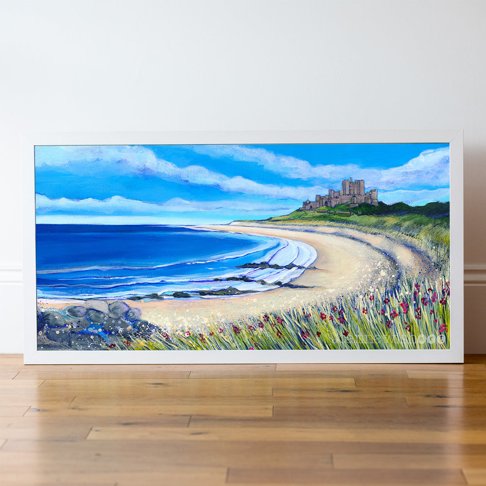 Framed painting of a coastal scene with a castle, beach, and flowers on a wooden floor.