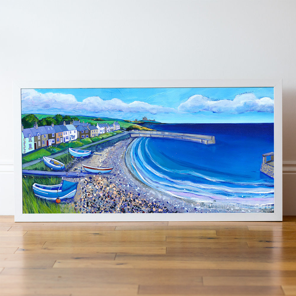 Framed artwork of a coastal scene with houses, boats, and waves on a white wall.