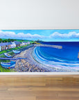 Framed artwork of a coastal scene with houses, boats, and waves on a white wall.