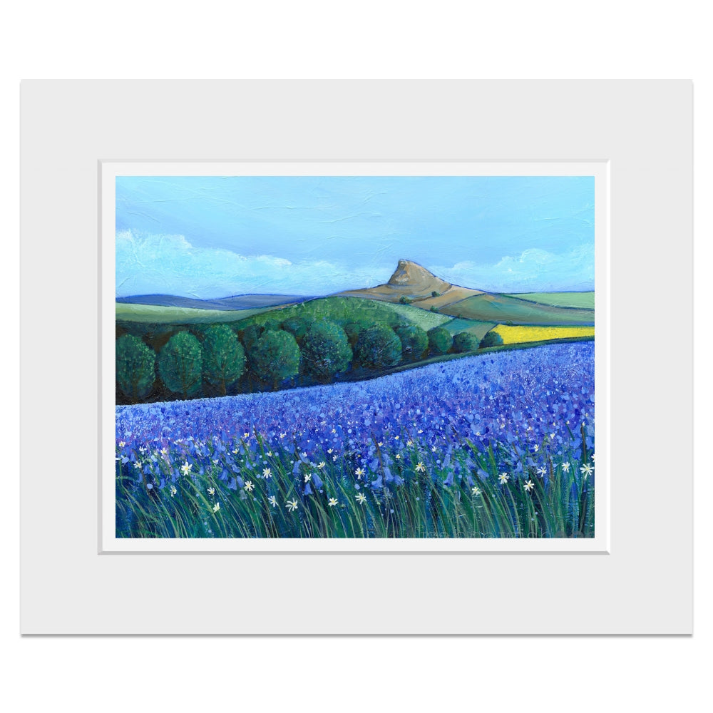 A mounted landscape painting featuring a vibrant purple lavender field in the foreground, green rolling hills and trees, and a brown mountain peak under a blue sky.