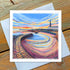A greetings card featuring an artistic print of Cullercoats Bay with a vibrant sunset and distant landmarks.