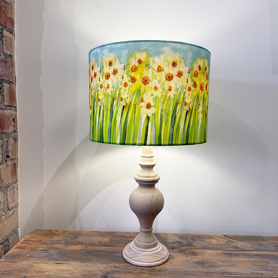 Lamp with floral daffodil design shade on a wooden table against a white wall.