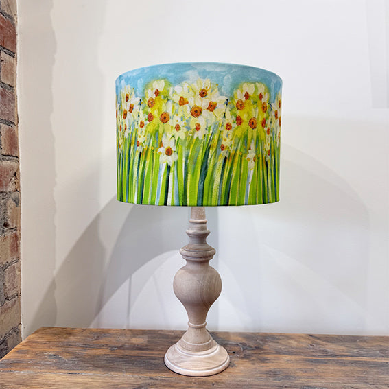 Lamp with a floral yellow daffodil design on the shade against a white wall.
