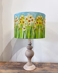 Lamp with a floral yellow daffodil design on the shade against a white wall.