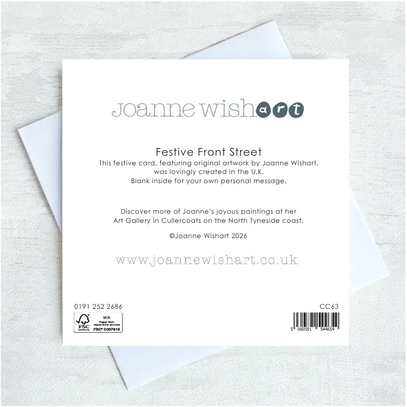 The back of a Joanne Wishart 'Festive Front Street' card, showing printed text, barcode, and recycling symbol, resting on top of a white envelope against a light gray textured background.