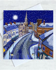 A square art print or card showing a snowy night tynemouth front street scene with buildings, a church spire, and a full moon, displayed over a white envelope on a light textured background.
