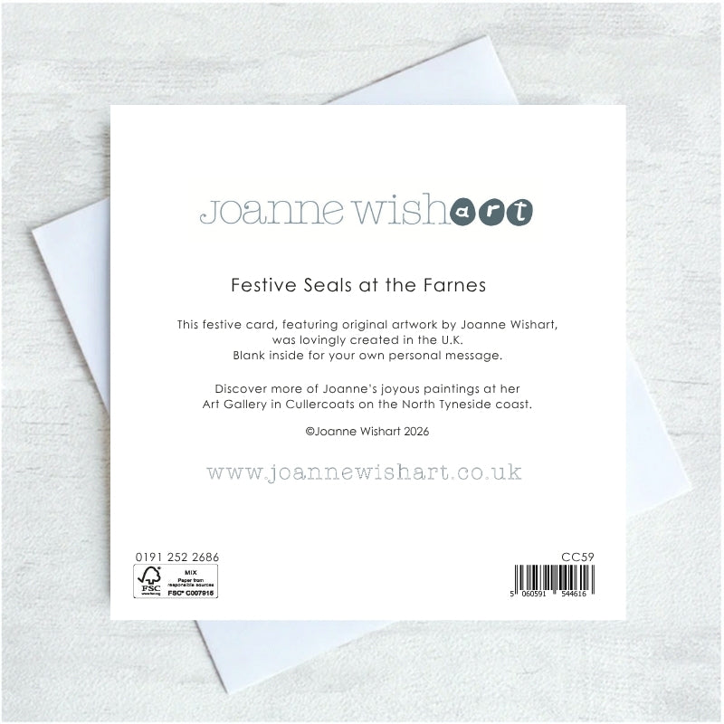 The back of a Joanne Wishart 'Festive Seals at the Farnes' greeting card, featuring product details, barcode, and text, displayed on top of a white envelope against a light gray textured background.