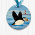 Round ornament with a puffin taking flight and lighthouse design on a blue background.