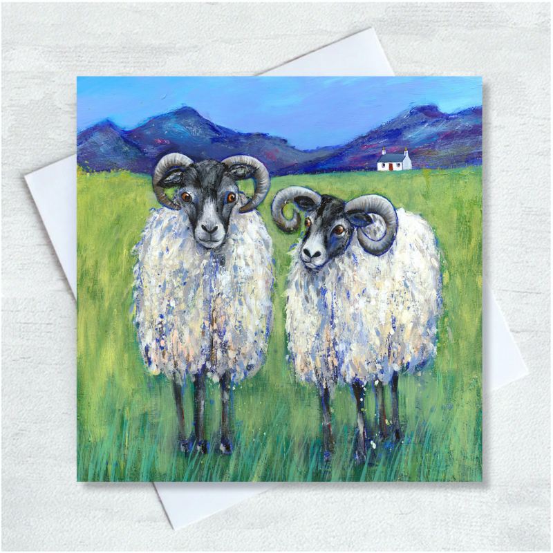 Two rams stand side by side on a grassy field against a blue sky, dark blue rocky mountains and a small white cottage.