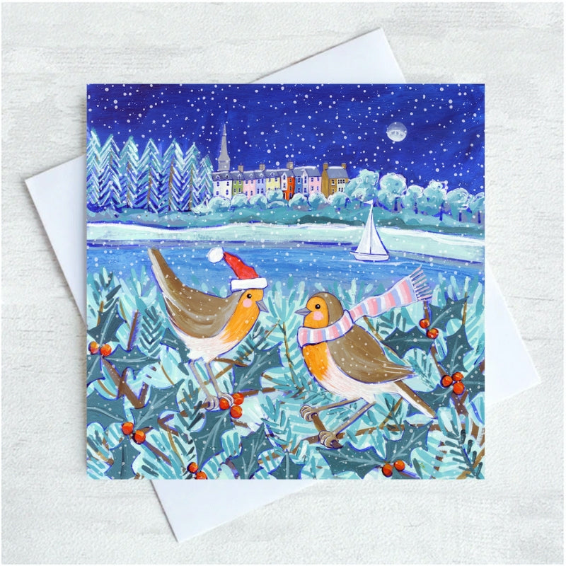 A christmas greeting card featuring two robins in the foreground with a snowy background and the houses of Alnmouth.