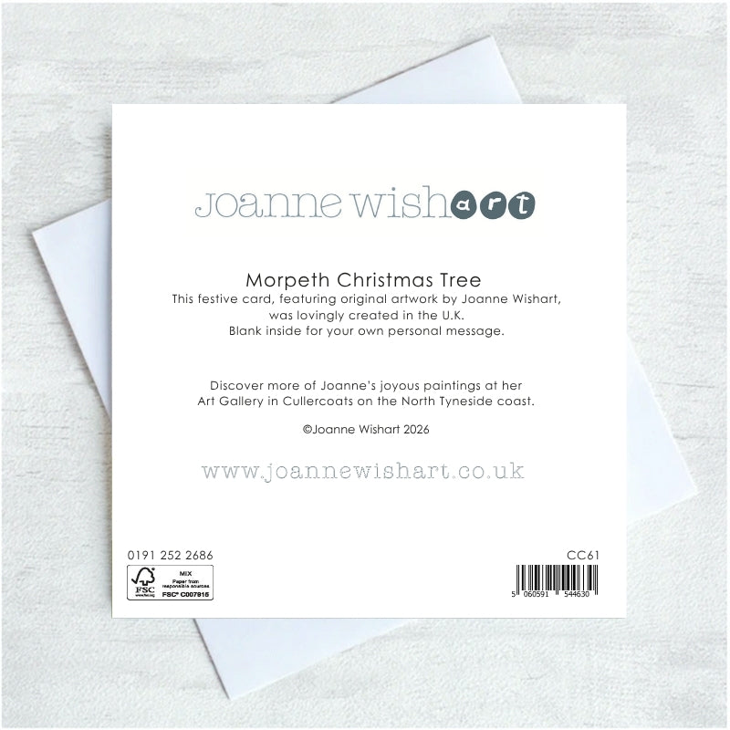 The back of a Joanne Wishart 'Morpeth Christmas Tree' greeting card, showing printed text, barcode, and recycling information, placed on top of white envelopes on a light gray textured background.
