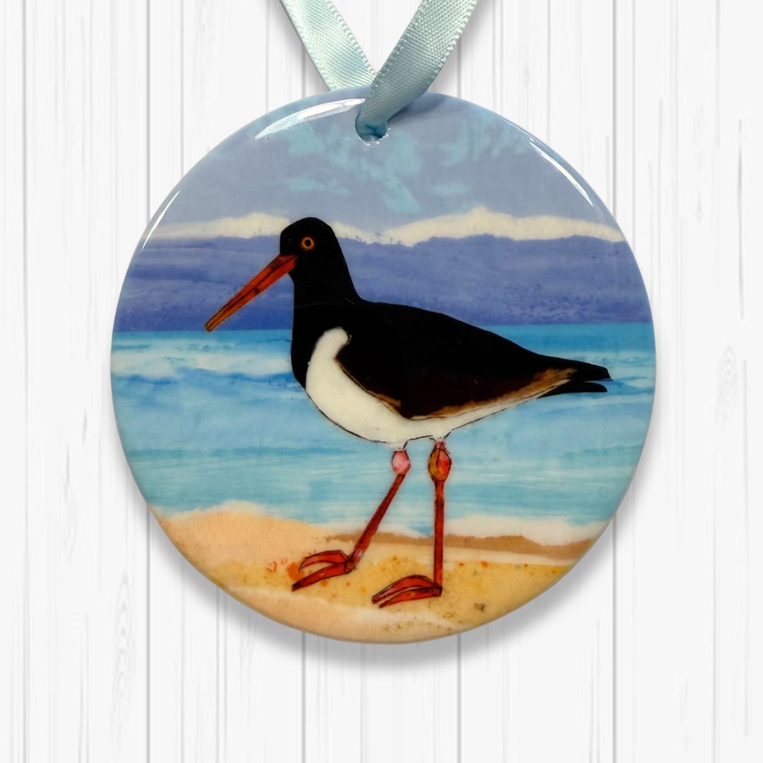 Decorative ornament with a Oyster catcher on a beach design, hanging on a white wooden surface.