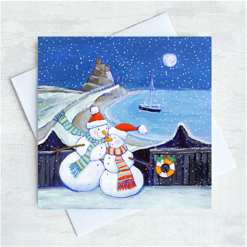 Two snowmen standing in front of the coast of lindisfarne with a castle in the background