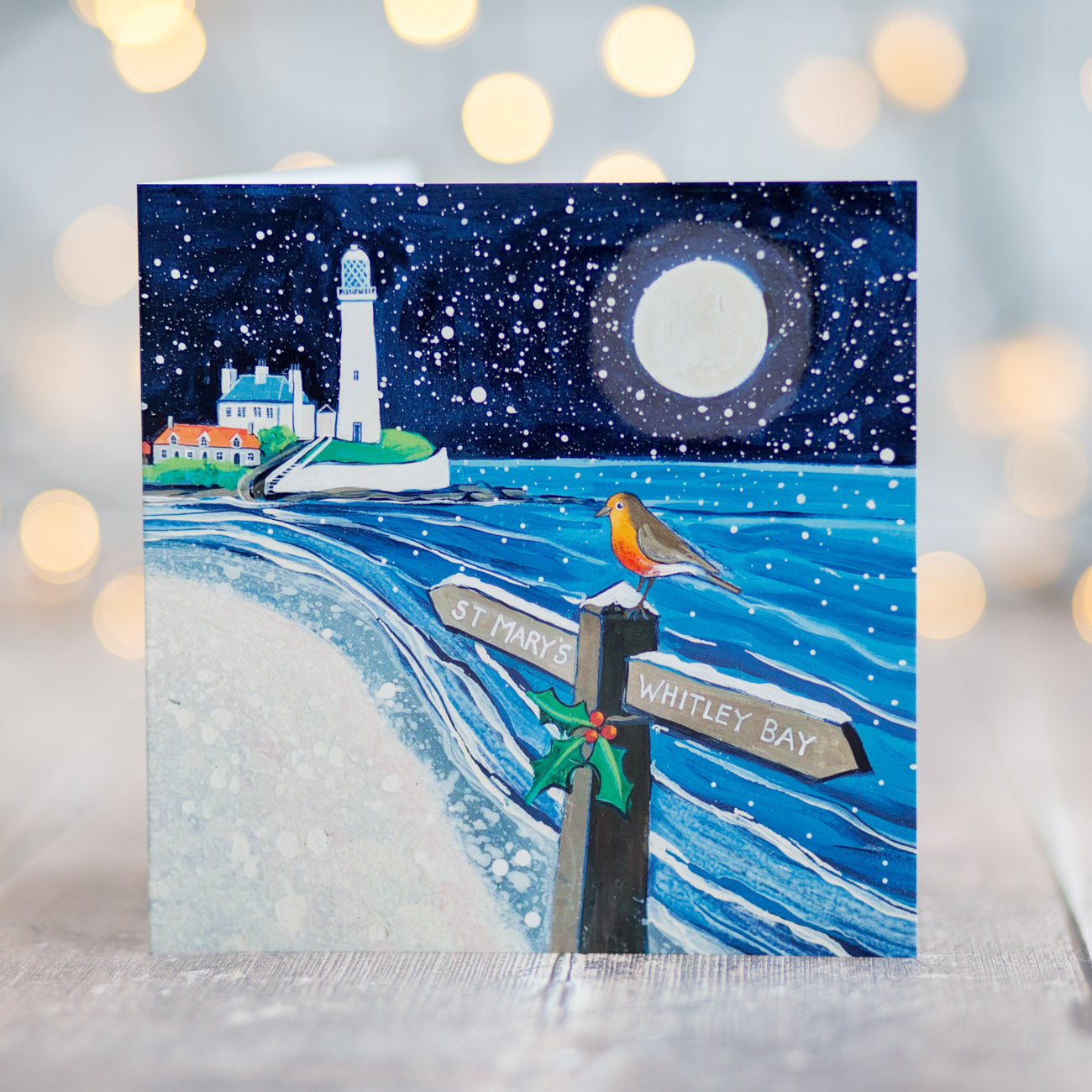 A greetings card featuring a white lighthouse  with a signpost directing people to St Mary's. A robin bird sits on top of the post. 