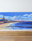 Framed artwork of a coastal scene with a church and beach on a white wall.
