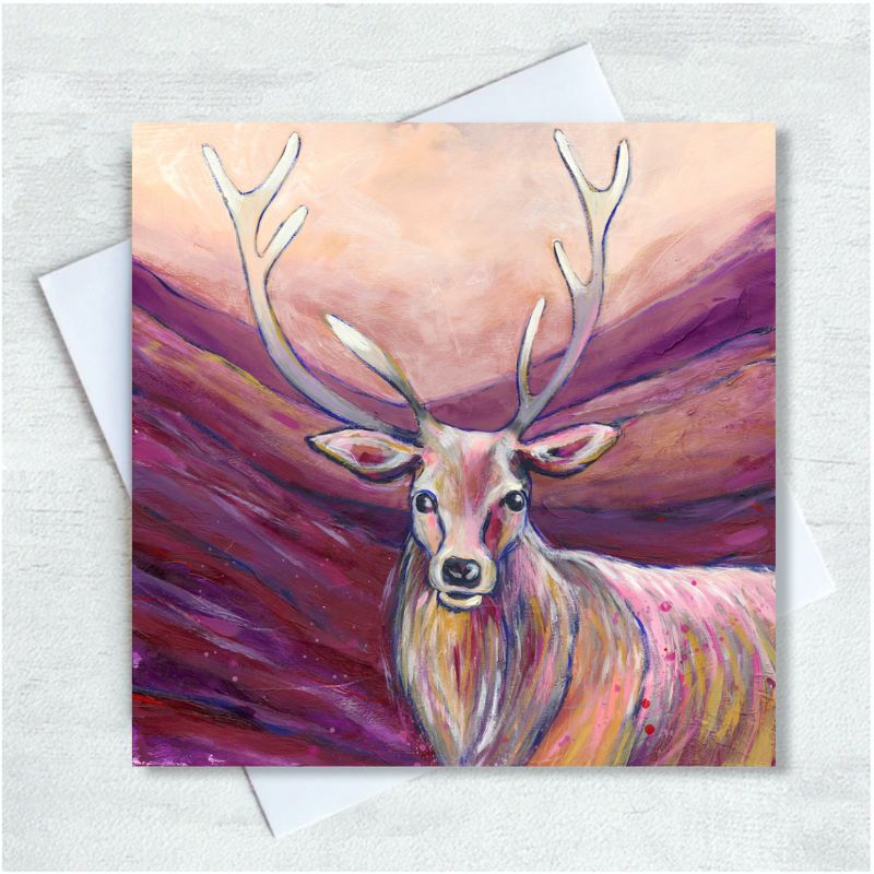 A brown stag stands looking out from a mauve and peach backdrop of a glen. 