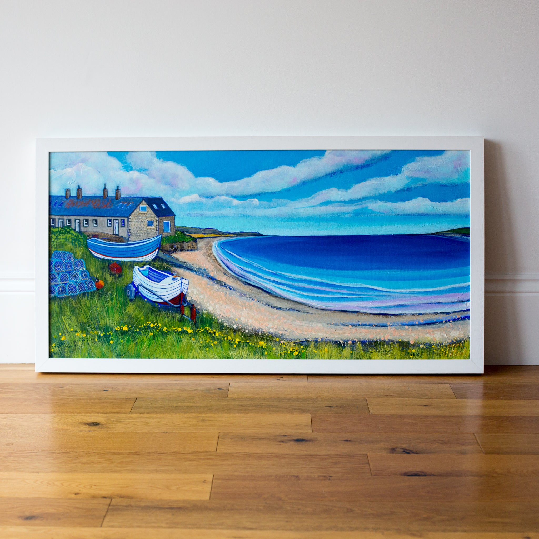 An original landscape painting of Boulmer Beach in Northumberland. Two coble fishing boats sit on the grassy shore in front of a row of old stone cottages,