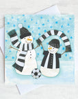 Two snowmen waving black and white scarfs in the snow. A Georde themed christmas Card with bright blue stars in the sky. 