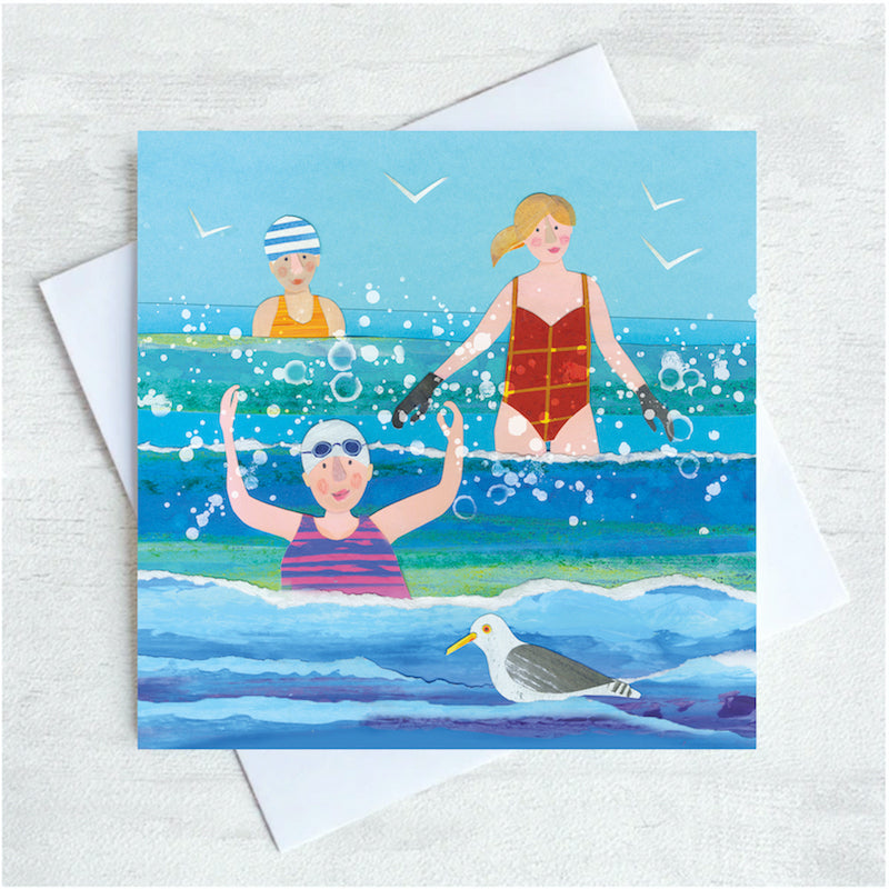 Three ladies and a seagull splash amongst the waves at the seaside. The are wearing broightly coloured swimsuits and have rosy red cheeks. 