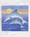 A greetings card featuring a leaping dolphin and calf at sunrise.