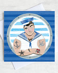 A greetings card featuring a tattooed sailing in uniform peeking through a ships porthole.