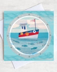 A greetings card featuring a cute fishing boat with fish swimming in the sea below.